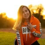 A woman smiling in a bright hoodie during the golden hour in a Rabat park.